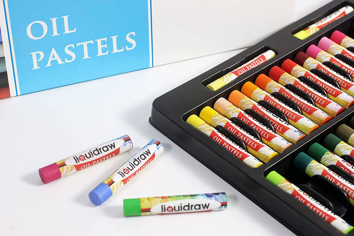 A set of colorful liquiddraw oil pastels arranged in a black tray on a white surface, with three loose pastel sticks placed in front and a blue box labeled OIL PASTELS in the background.