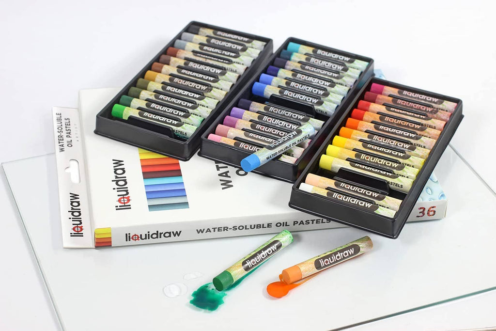 A set of 36 Liquiddraw water-soluble oil pastels in multiple colors, arranged in three black trays on top of their product box, with two loose pastels lying in front on a white surface.