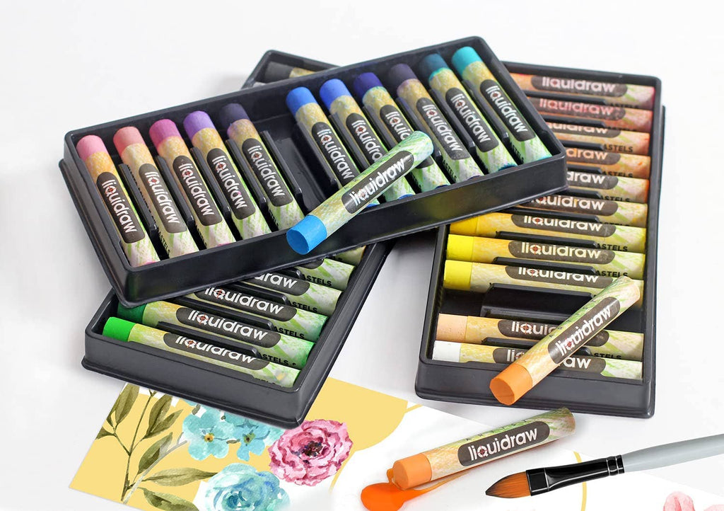 Three black plastic trays of liquiddraw liquid pastels arranged on a white surface, with a paintbrush and a few painted paper swatches nearby. The pastels show a variety of colors including pink, blue, green, yellow, orange, and purple.