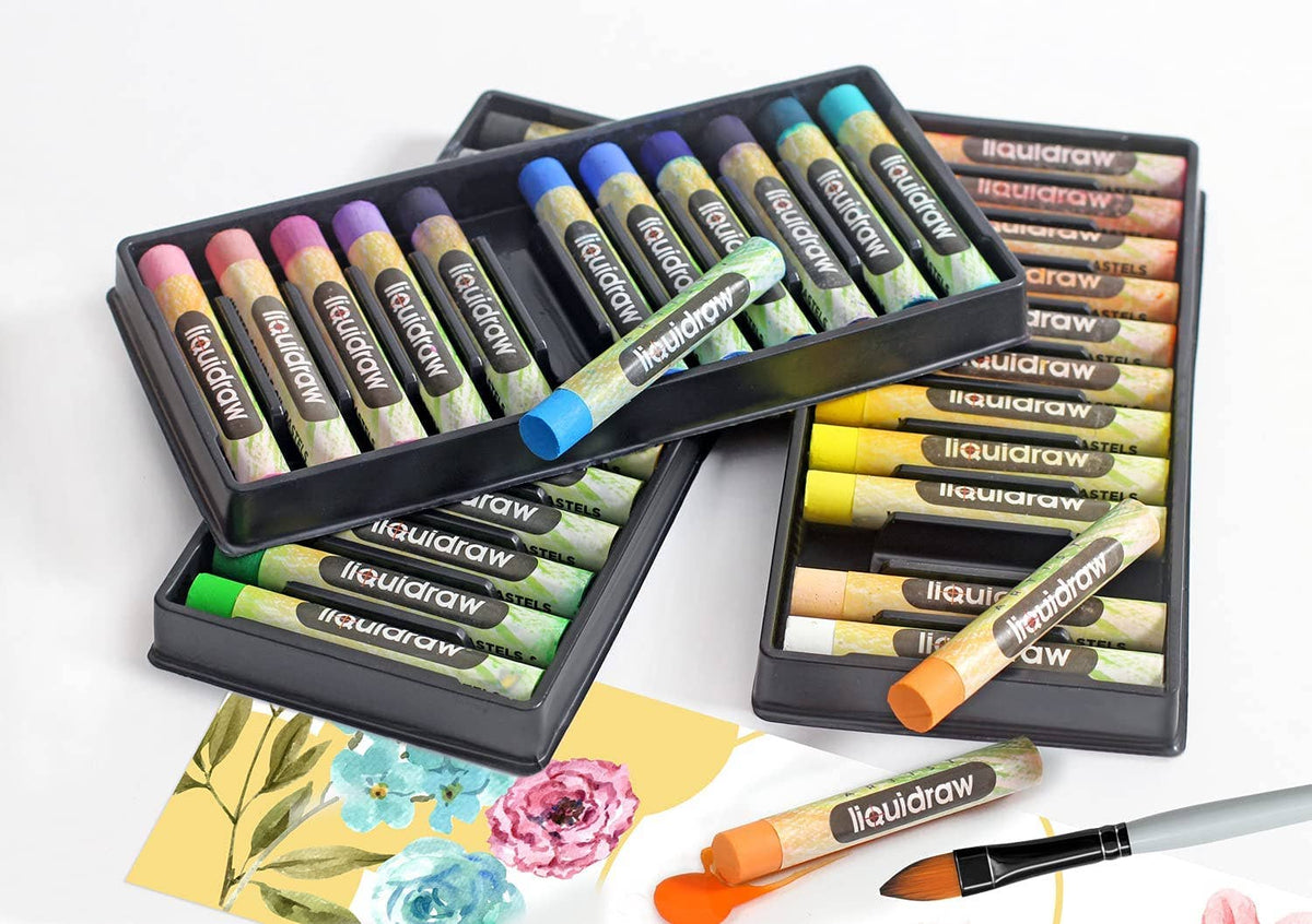 Three black plastic trays of liquiddraw liquid pastels arranged on a white surface, with a paintbrush and a few painted paper swatches nearby. The pastels show a variety of colors including pink, blue, green, yellow, orange, and purple.