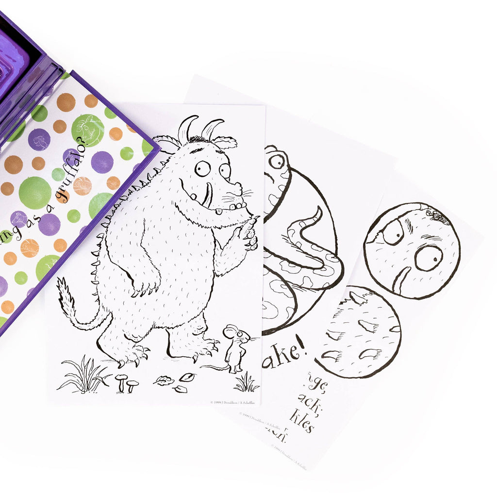 A children's Gruffalo colouring book or colouring page set shown on a white background, featuring a black-and-white monster illustration, circular face stickers, and part of a purple patterned box.