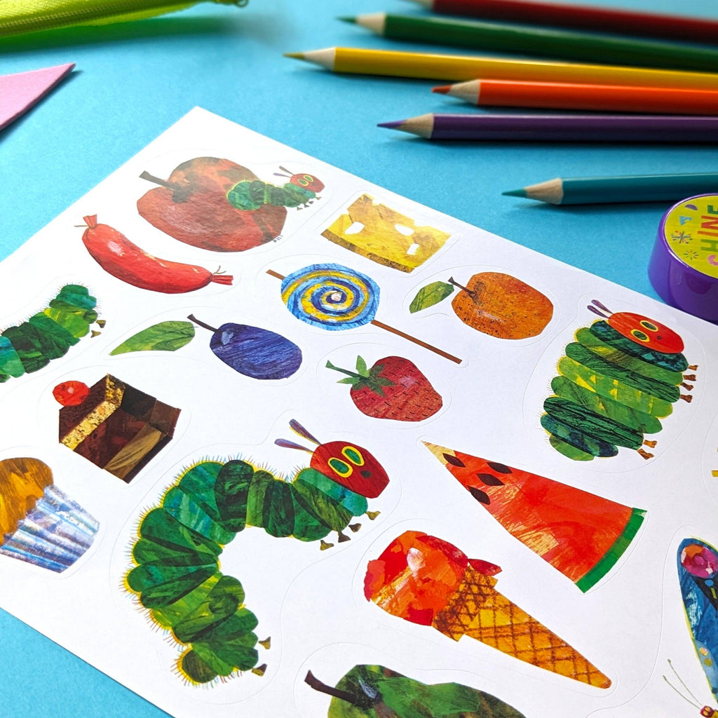 Colourful stickers of caterpillars and fruits on a blue surface with pencils.