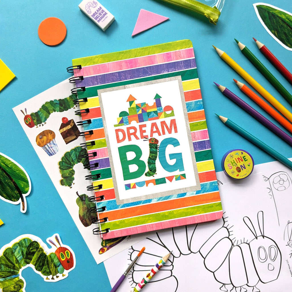 Colourful notebook with 'Dream Big' design surrounded by art supplies on a blue background