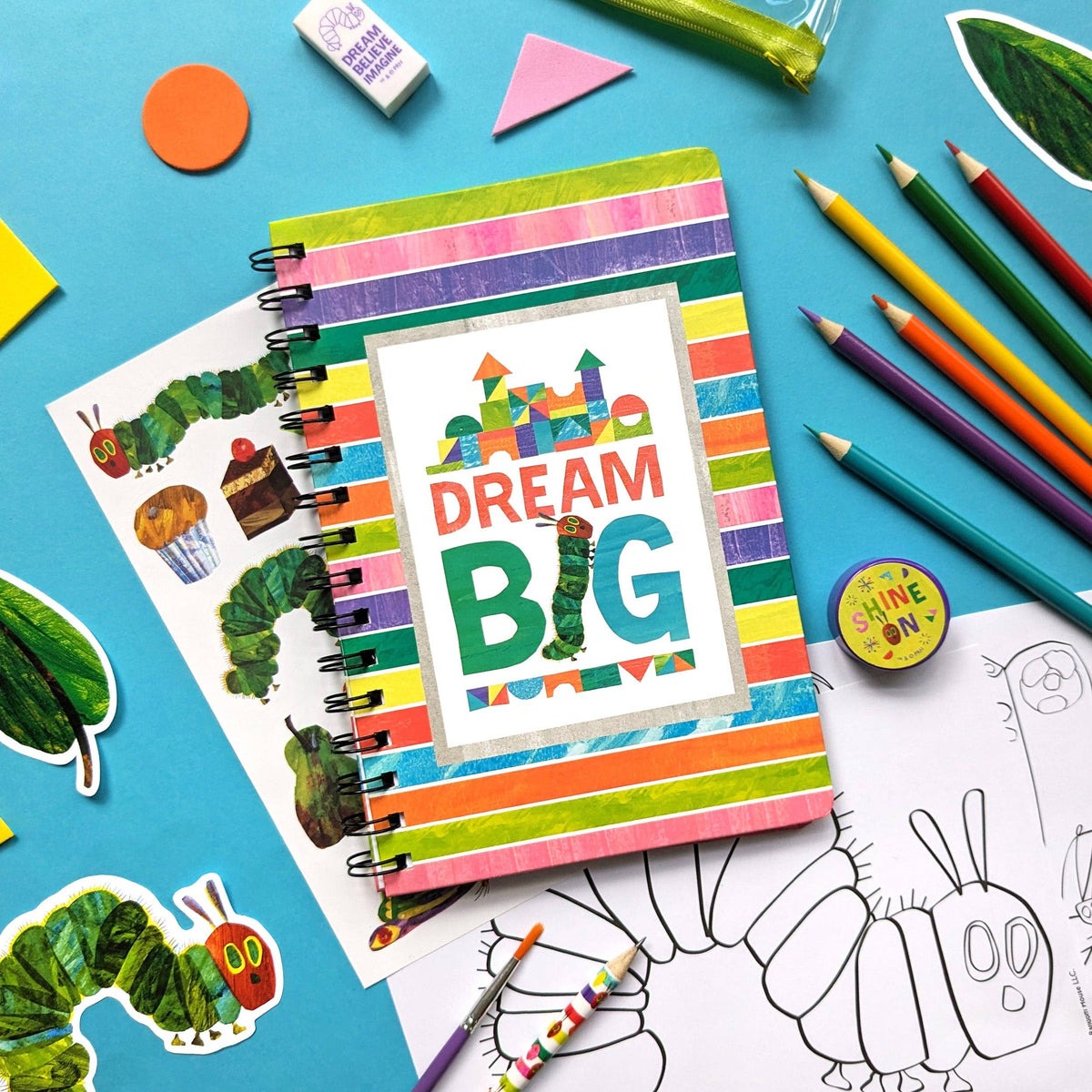 Colourful notebook with 'Dream Big' design surrounded by art supplies on a blue background