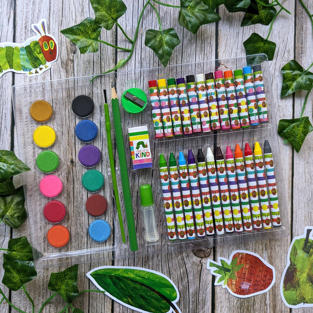 Assorted art supplies including crayons, watercolours, and markers on a wooden surface with leaves.