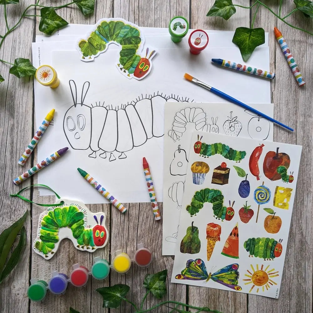 Coloring sheets and craft materials on a wooden surface with illustrations of a caterpillar and leaves.