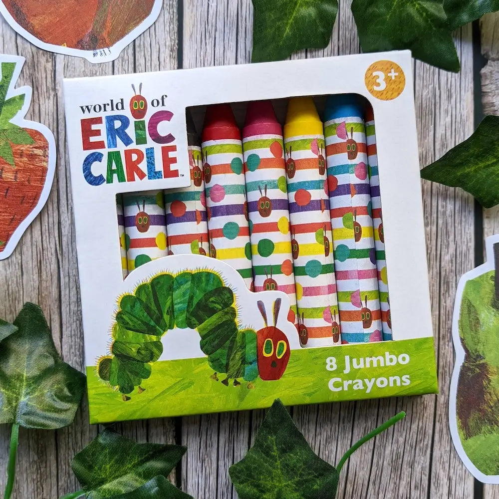 Box of crayons with 'World of Eric Carle' branding on a wooden surface with leaves.